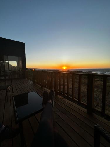 a person sitting on a deck watching the sunset at Casa Olas, Refugio Costero in Curanipe