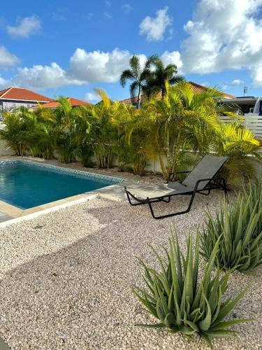 a chair next to a swimming pool with palm trees at Villa Vista Montaña in Willemstad