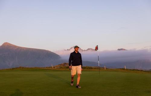 a man standing on a golf course with mountains in the background at Luksushytte sentralt i Lofoten in Kleppstad