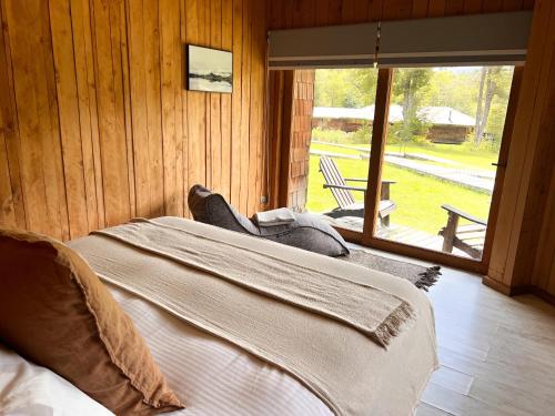a bed in a wooden room with a large window at Peuma Lodge Patagonia in Futaleufú