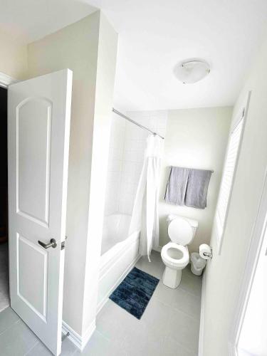 a white bathroom with a toilet and a bath tub at Large 5 Bedroom Newly Built Home Sleeps 12 Persons in Thorold