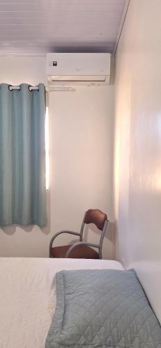 a bedroom with a bed and a chair next to a window at Kitnet em Imbituba - Fabi in Imbituba