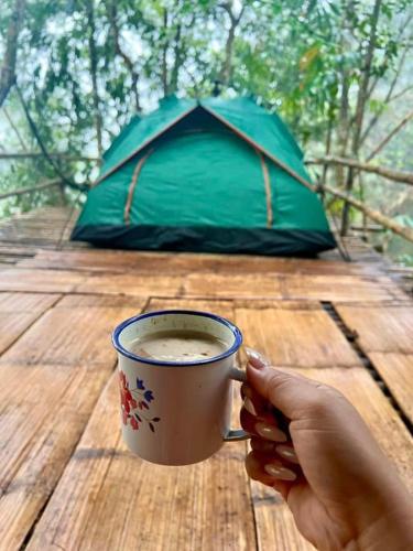 a person holding a cup of coffee on a wooden table at Baruk Mas Kampung Assum in Kuching