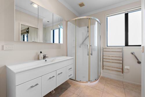 a white bathroom with a shower and a sink at Sun, Sand, Serenity - Waihi Beach Holiday Home in Waihi Beach