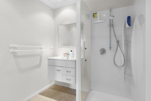 a white bathroom with a shower and a sink at Sun, Sand, Serenity - Waihi Beach Holiday Home in Waihi Beach
