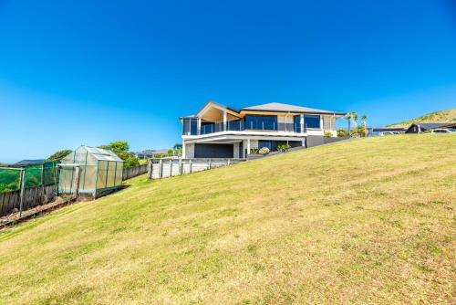 a house on top of a grassy hill at Sun, Sand, Serenity - Waihi Beach Holiday Home in Waihi Beach