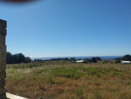 a view of a field with the ocean in the background at Cabañas encanto de Chovellen in Pelluhue