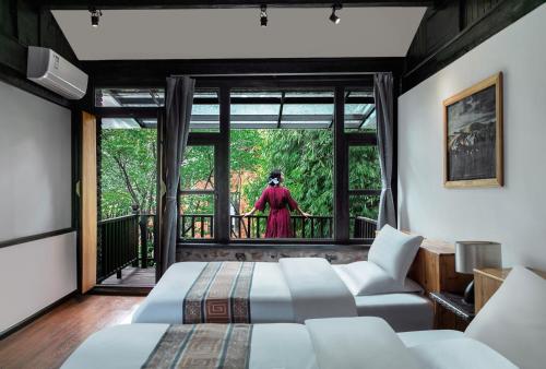 a room with two beds and a woman standing outside the window at 阅时 Adonis野生派 Black Bar 森林大院民宿 in Lijiang