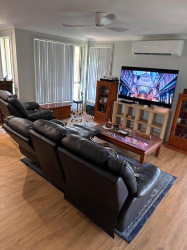 a living room with black leather furniture and a flat screen tv at Coastal Calm Entire Top Floor of House Private Entrance and ammenities in South West Rocks