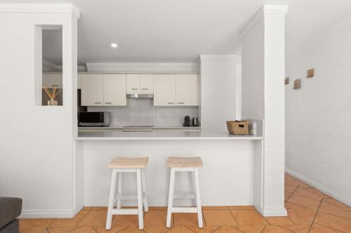 a kitchen with two bar stools and white cabinets at Greenheyes on Currambene by Experience Jervis Bay in Huskisson