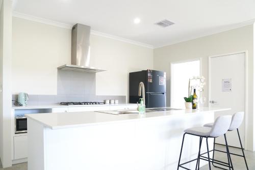 a white kitchen with a counter and two bar stools at StayAU 5BRM Coastal Retreat for Families Baldivis in Baldivis