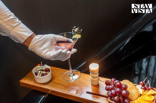 a person holding a glass of wine on a table with fruit at The Den by Vieda - Part of StayVista in Karjat