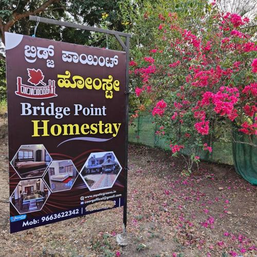 a sign for a bridge point homesteadery next to flowers at MysticGreens Guest House! in Kushālnagar