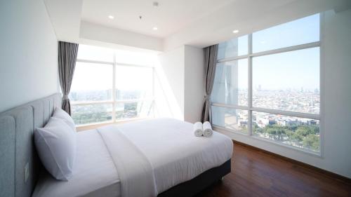 a bedroom with a white bed and a large window at Exclusive and Spacey 3BR at Grand Sungkono Lagoon Apartment By Travelio in Surabaya