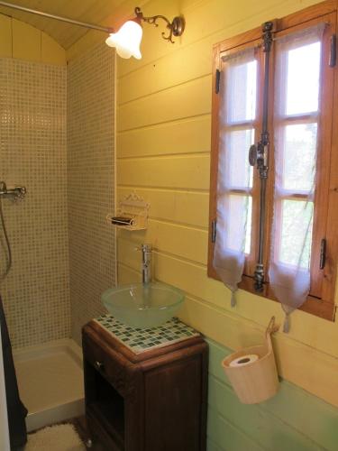 La salle de bains est pourvue d'un lavabo en verre et d'une fenêtre. dans l'établissement Les Roulottes Du Lauragais, à Montmaur