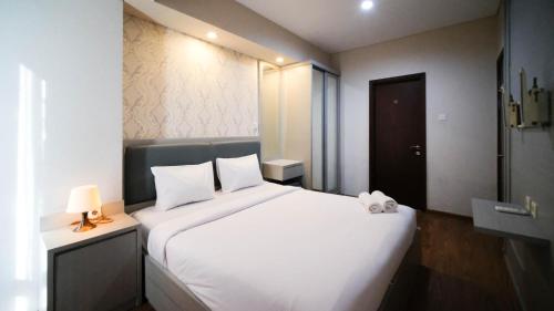 a bedroom with a large white bed with a teddy bear on it at Modern and Cozy 1BR at Grand Sungkono Lagoon Apartment By Travelio in Surabaya