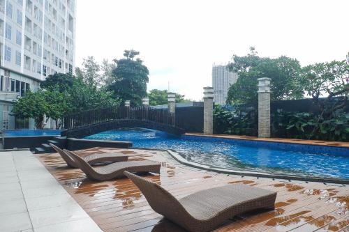 a swimming pool with lounge chairs in a city at Modern and Cozy 1BR at Grand Sungkono Lagoon Apartment By Travelio in Surabaya