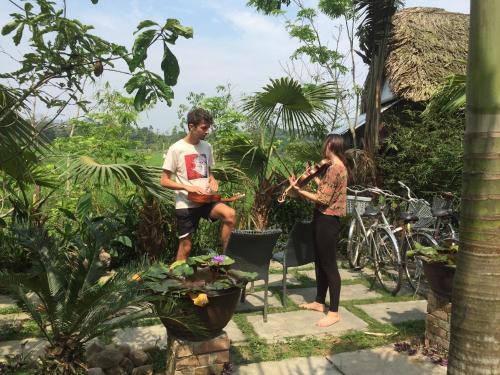 a man and a woman playing instruments in a garden at Vuglamping in Hue