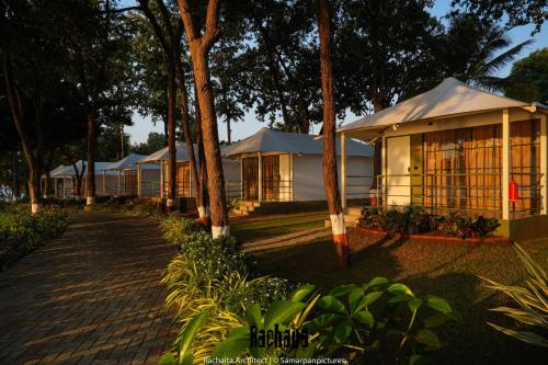 a row of white tents with trees and a sidewalk at White Feather Resort Kauncha in Silvassa