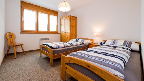 a bedroom with two beds and a window and a chair at Christiania in Riederalp