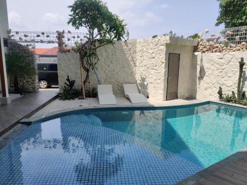 a swimming pool with two chairs next to a building at HŌM Coliving Bali in Kerobokan