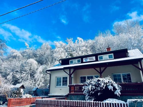 a white house with snow covered trees in the background at Penzion U Rodinky in Bělá pod Pradědem