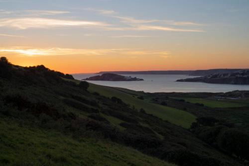 a sunset on a hill with a view of the ocean at Badgers Den, a beautiful log cabin in a secluded valley close to the beach in Bantham