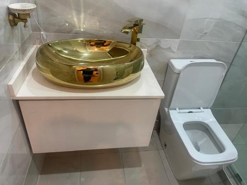 a bathroom with a gold sink and a toilet at Tropical Enclave Apartment Osu in Accra