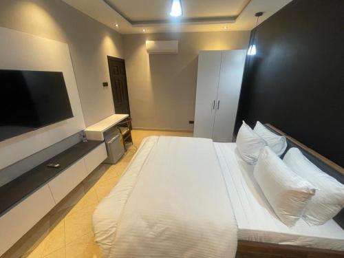 a bedroom with a large white bed with a flat screen tv at Tropical Enclave Apartment Osu in Accra