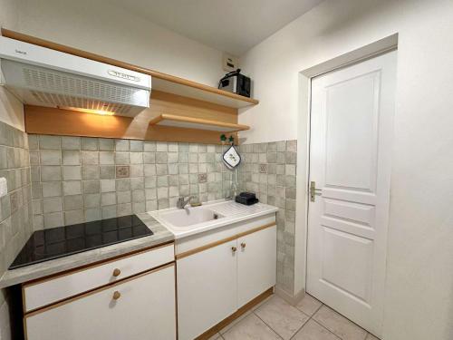 Elle comprend une petite cuisine avec un évier et une porte blanche. dans l'établissement HYEGUY Appartement pour 3 personnes en rez de jardin avec piscine commune à Giens, à Hyères