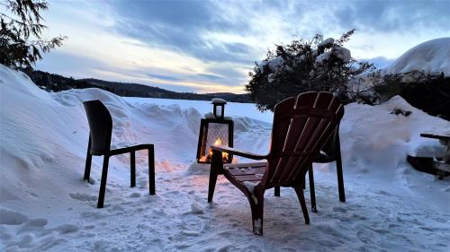 two chairs and a candle in the snow at Le1617 - Quai privé, Lac-Les chalets dans le nord in Sainte-Lucie-de-Doncaster