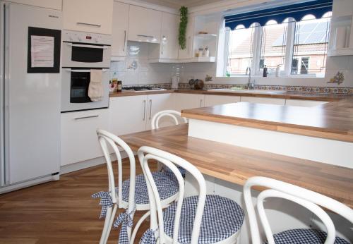 a kitchen with white cabinets and a wooden table with chairs at The Bungalow at Parkside, 4 ensuite bedrooms in Goole
