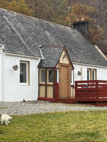 a small white house with a dog laying in front of it at Loch Maree Hotel in Talladale
