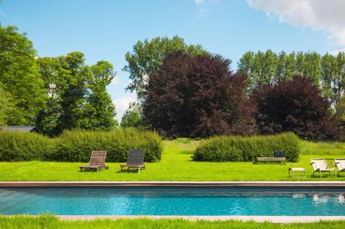 a swimming pool with two chairs and a group of trees at Domaine des Chanoines blancs in Gouy-Saint-André