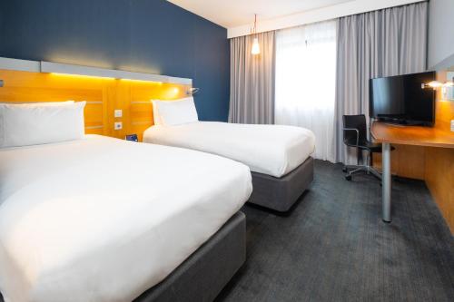 a hotel room with two beds and a desk and a tv at Holiday Inn Express Stevenage by IHG in Stevenage