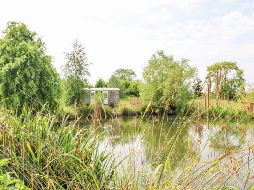a house in a field next to a body of water at Herbie's Shepherds Hut at Shepherds Lodge Retreat and Wellness in Nottingham