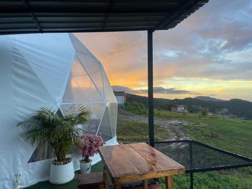 a glass tent with a wooden table and flowers on a patio at Tubburk glamping VIP in Ban Maeo Thap Boek
