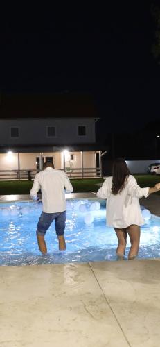 two people standing in a swimming pool at night at Vila Marra in Čurug
