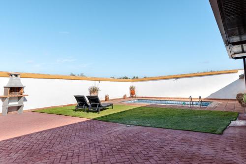 een terras met twee stoelen op een gazon met een zwembad bij Casa rural con piscina, barbacoa, aire acondicionado, WiFi de alta velocidad, cocina exterior y Parking in Córdoba