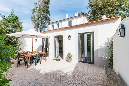 a white house with a table and an umbrella at Vila Santa Maria - Cosy Guest House in Sintra