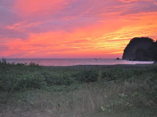 a sunset on a beach with a rock in the ocean at Pension Surf Rider in Nishiizu
