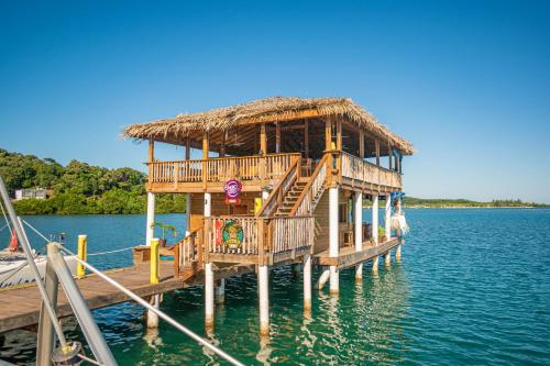 a wooden pier with a thatched house on the water at Wikkid Resort in Dixon Cove