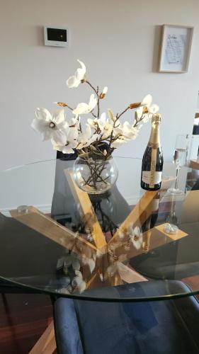 a glass table with a vase of flowers and a bottle of wine at Capel Sands Beachfront Apartment in Capel Sound