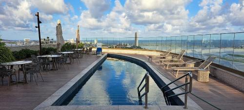 a swimming pool on top of a building with tables and chairs at Parque do Cais - Flats Premium no Recife por Yolo in Recife