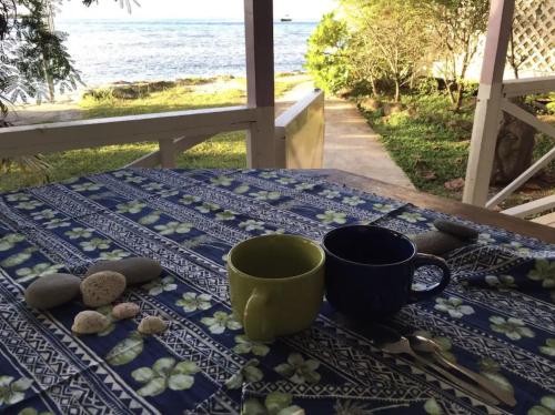 a table with two coffee cups on a table with the beach at Te fare iti - Bungalow bord de mer in Maharepa
