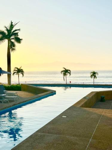 a swimming pool next to the ocean with palm trees at Beautiful Oceanview Apartment in Zantamar in Cruz de Huanacaxtle
