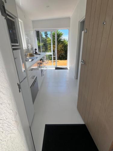 a kitchen with white tile flooring and a hallway with a door at Sunny hillside central Nelson hideaway with city to sea views in Nelson