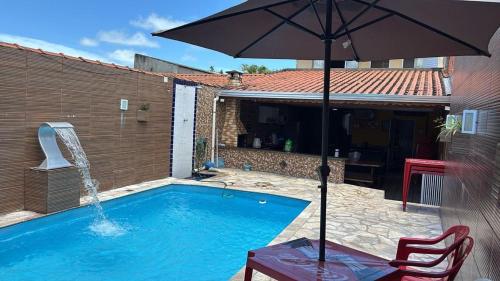 a swimming pool with an umbrella and a table and a chair at Piscina, Churrasqueira, Ar Condicionado e 3 Vagas de Garagem in Mongaguá
