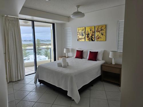 a bedroom with a bed with red pillows and a window at The Waterford Prestige Apartments in Caloundra