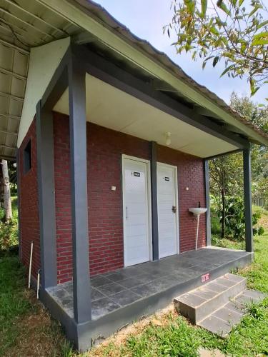 a brick building with two white doors and a porch at Kebun Teduh Sukaharja Cijeruk Bogor in Palasari